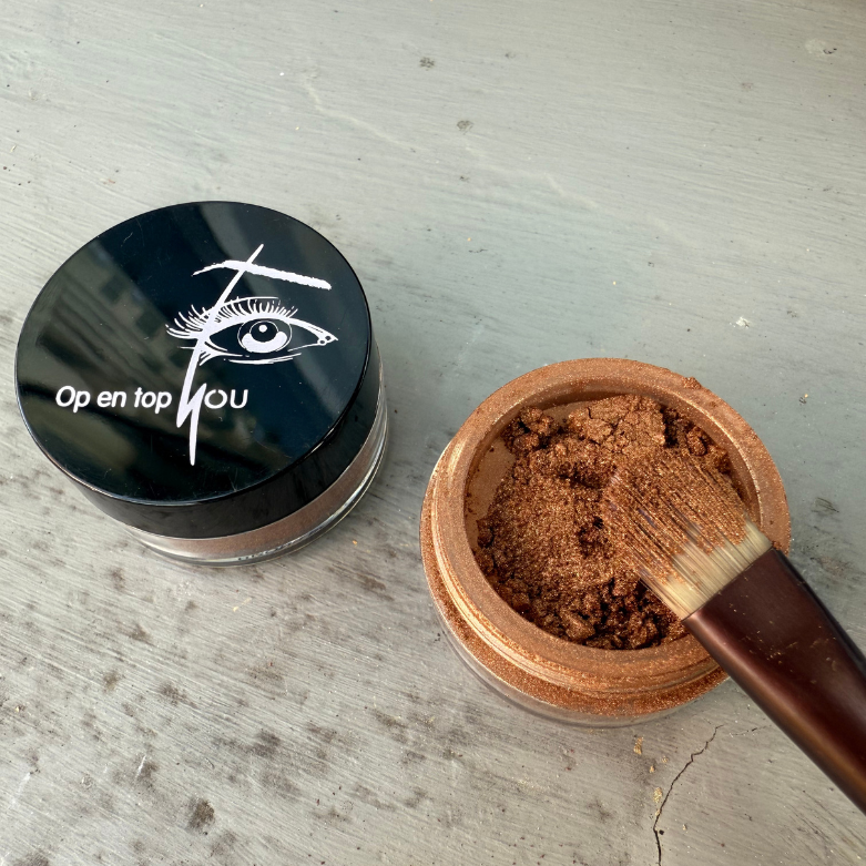 Een klein rond potje minerale oogschaduw in de kleur Koper Kos, een bruine kopertint met een gouden gloed en een subtiele glans, in een losse, poederige textuur.